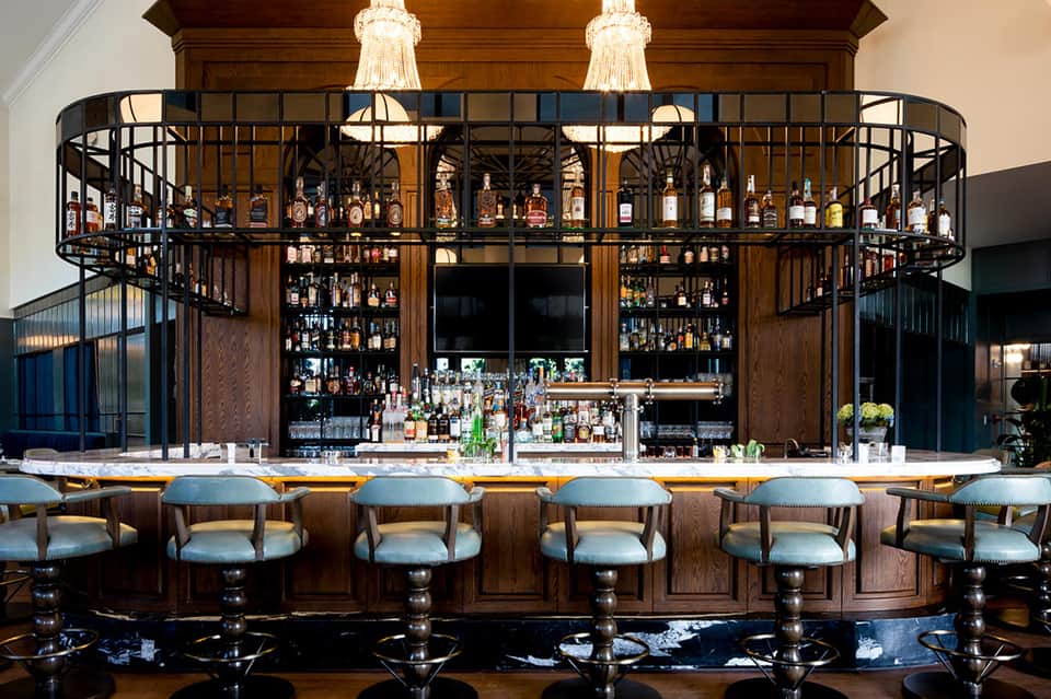 Elegant curved bar with wood paneling, blue upholstered stools, and extensive liquor collection