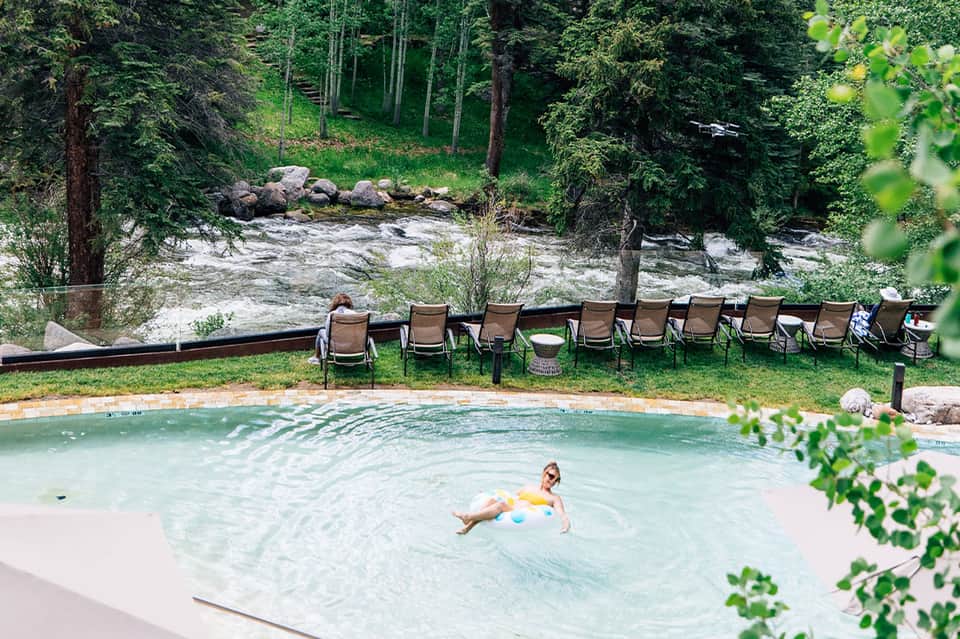Natural hot spring pool surrounded by forest, river, and lounge chairs