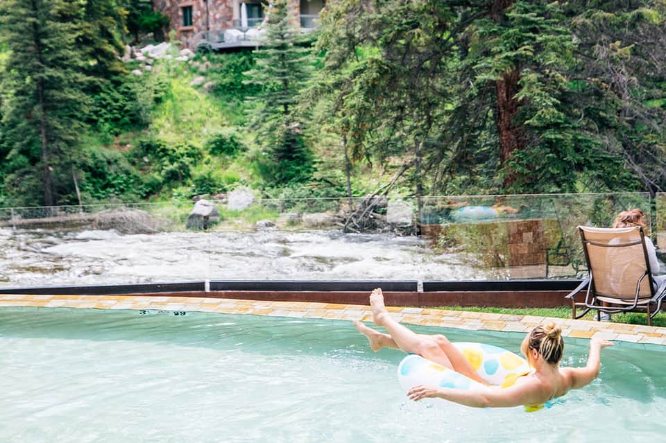 Guest floating on colorful pool float in natural hot spring surrounded by forest and mountain landscape