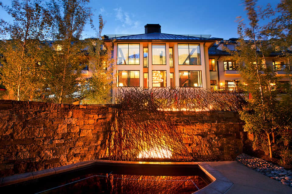 Modern building exterior at dusk with warm lighting, surrounded by birch trees and illuminated landscape
