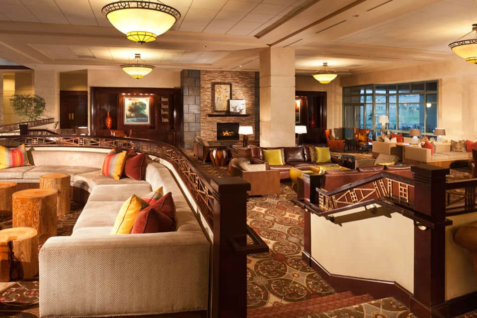 Upscale hotel lobby lounge with wood furnishings, fireplace, earth-tone decor, and warm lighting