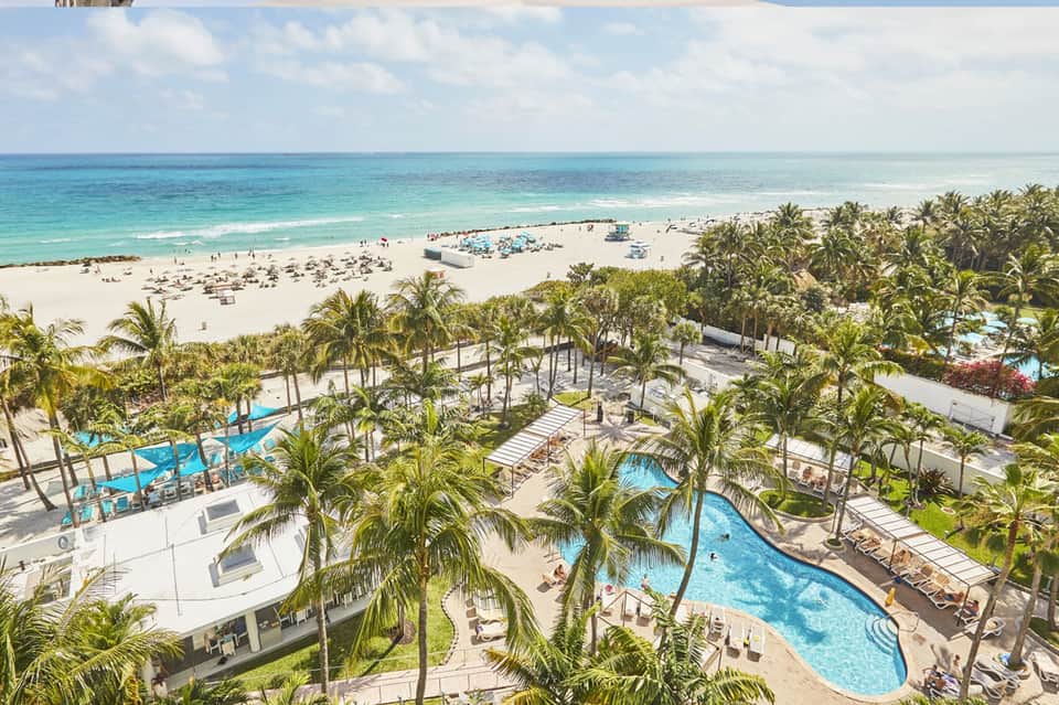 Aerial view of beachfront resort with pools, palm trees, pristine beach, and turquoise ocean