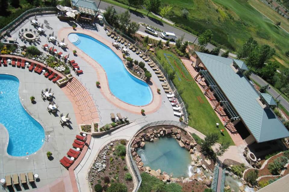 Aerial view of resort pools, hot tub, loungers, and manicured grounds on hillside