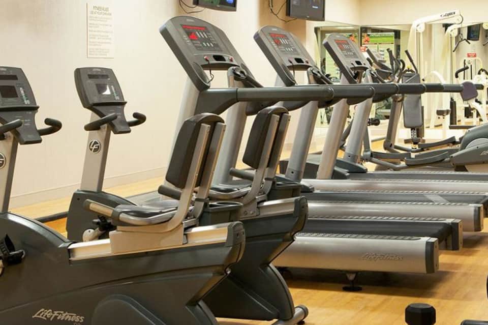 Fitness center with rows of exercise bikes and cardio equipment along white wall