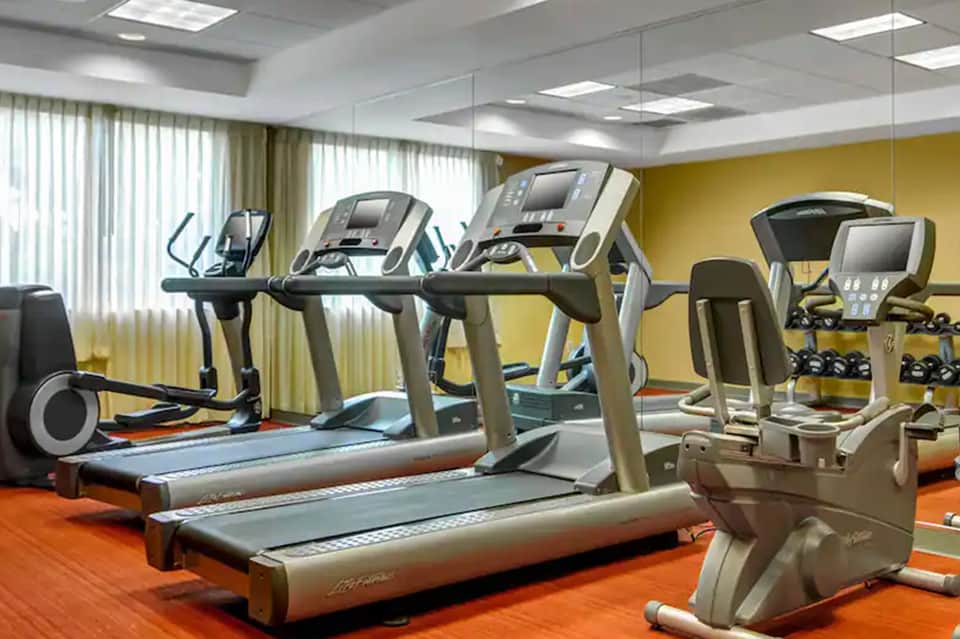 Fitness center with treadmills and exercise equipment against yellow accent wall and windows