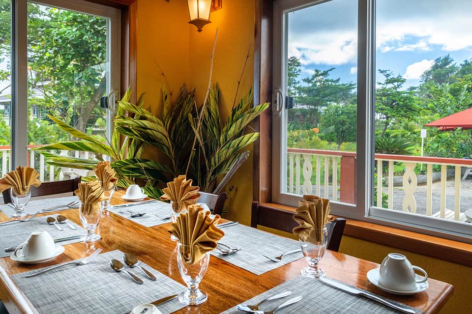 Dining room with orange accent wall, elegant table settings, and tropical forest views