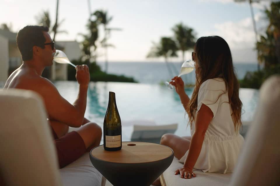 Couple enjoying wine and ocean view while relaxing by infinity pool at beachfront resort