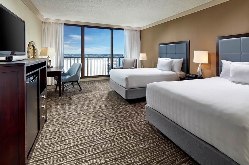 Hotel double queen room with balcony view, work desk, and modern furnishings