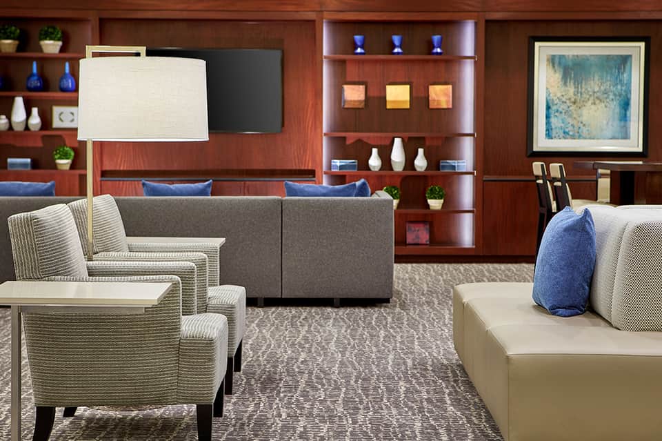 Hotel lounge with wood paneling, comfortable seating, fireplace, shelving, and blue accent pillows