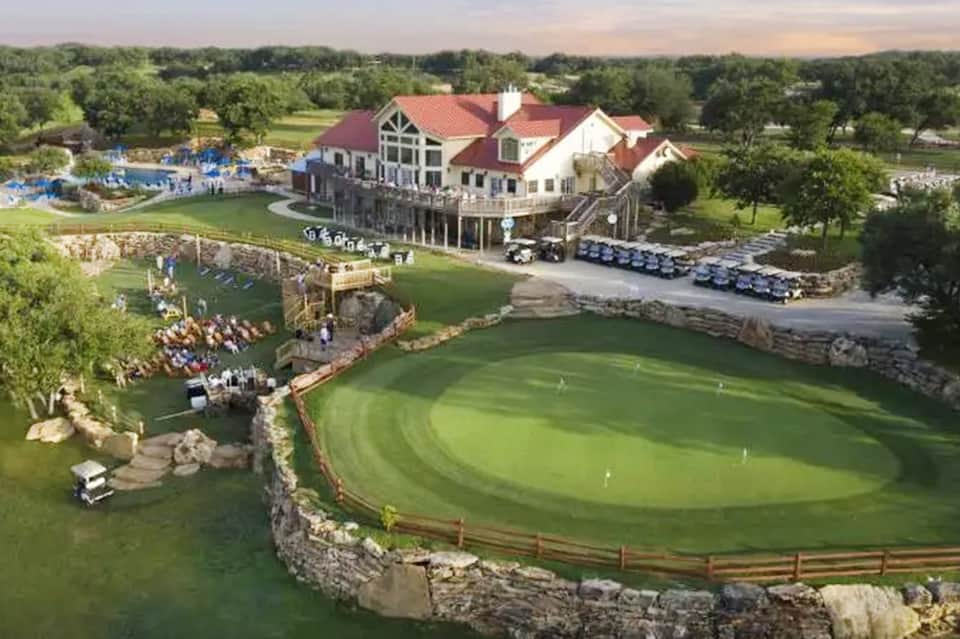 Aerial view of luxury resort with large mansion, golf course, water features, and manicured grounds.