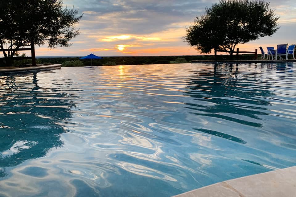 Resort infinity pool at sunset reflecting golden sky with lounge chairs and ocean horizon view