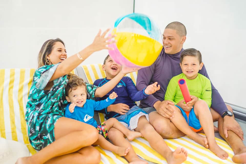 Family of five playing with colorful beach ball on striped lounge chair indoors