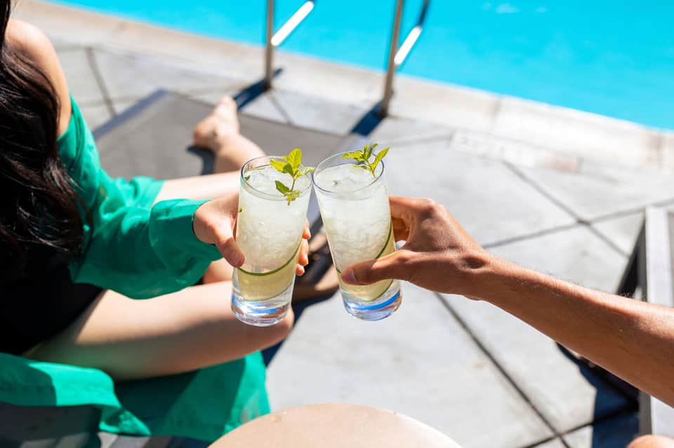Two people toasting with clear cocktails by bright blue swimming pool