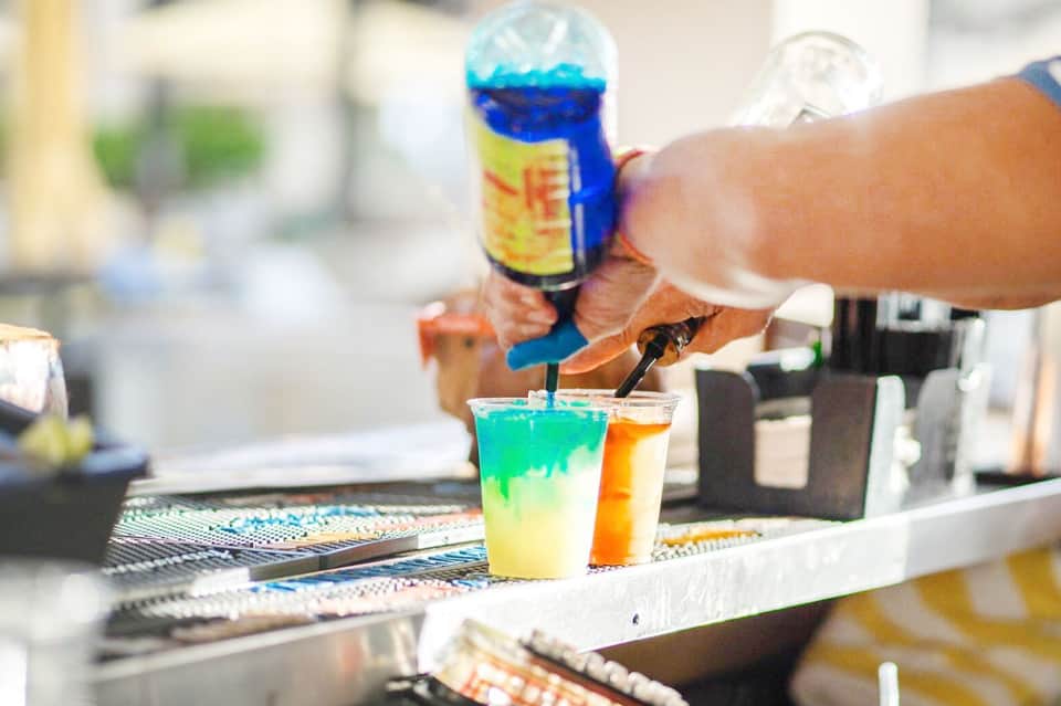 Bartender pouring colorful layered cocktails at an outdoor bar station