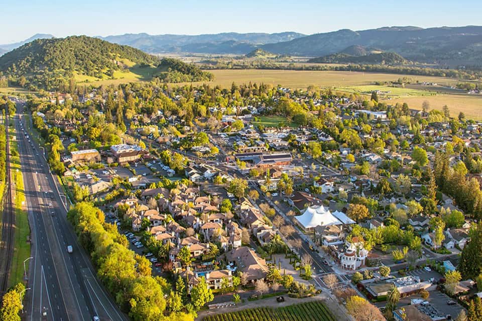 Aerial view of suburban residential community nestled among green hills and farmland with highway on left