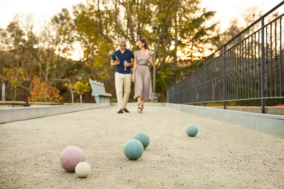 Bocce ball court with colored balls in foreground and couple jogging in background