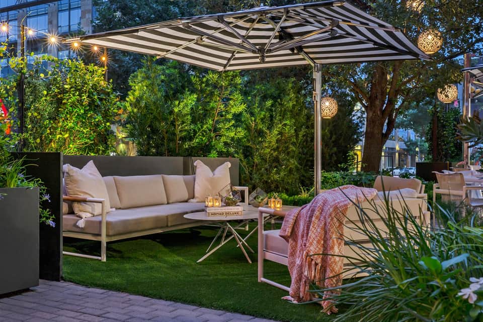 Modern outdoor lounge with striped canopy, sofa, and ambient pendant lighting