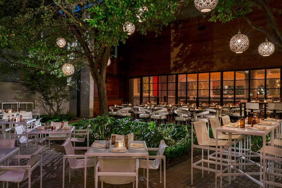Upscale outdoor restaurant courtyard with ambient lighting, lush greenery, and modern seating