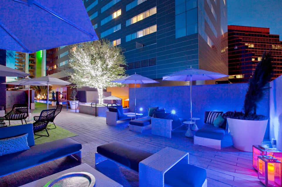 Modern rooftop terrace with blue uplighting, lounge seating, umbrellas, and downtown city views
