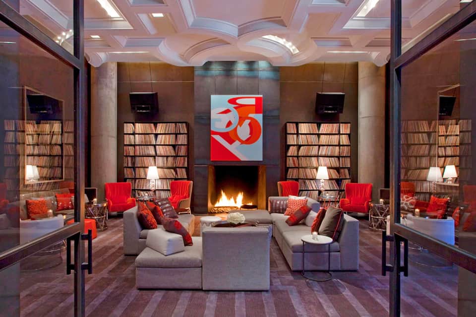 Upscale lounge with fireplace, red chairs, bookshelves, and artistic ceiling design