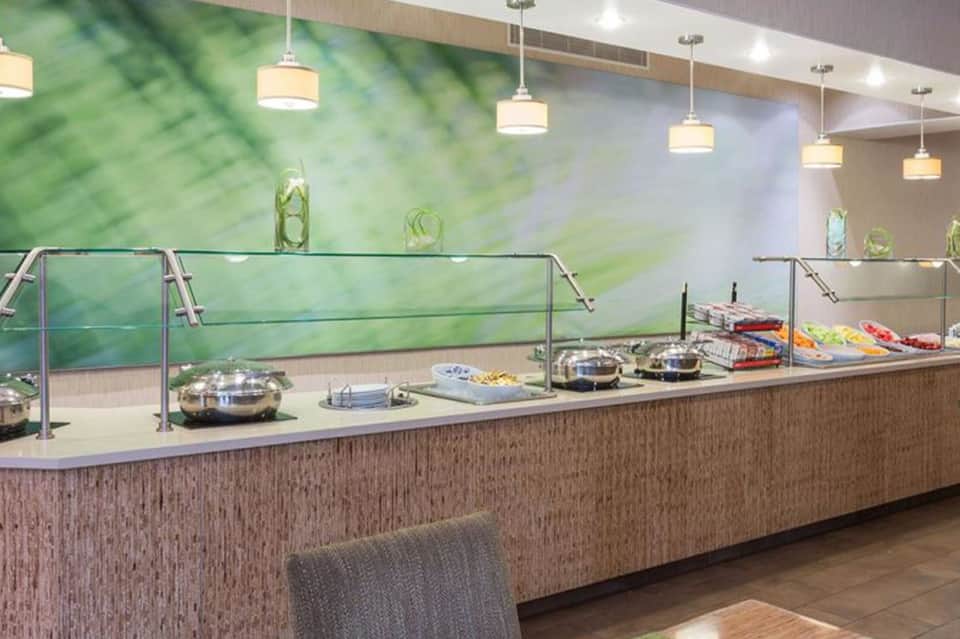 Buffet service counter with glass sneeze guard and warming trays under pendant lighting