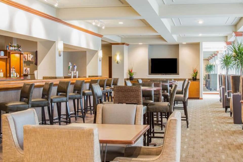 Hotel lounge with bar counter, high seating, wooden accents, and entertainment space