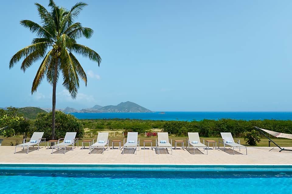 Resort pool with white lounge chairs, palm tree, and volcanic island ocean view