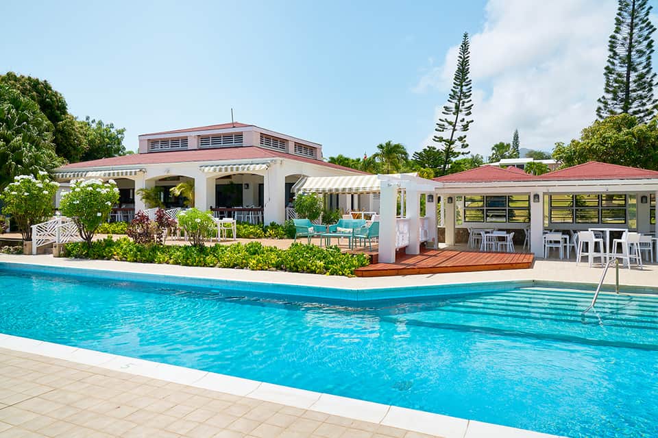 Resort pool facility with white main building, turquoise water, and tropical vegetation