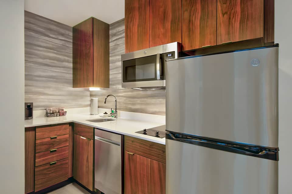 Modern kitchenette with stainless steel appliances, wood cabinetry, and tile backsplash