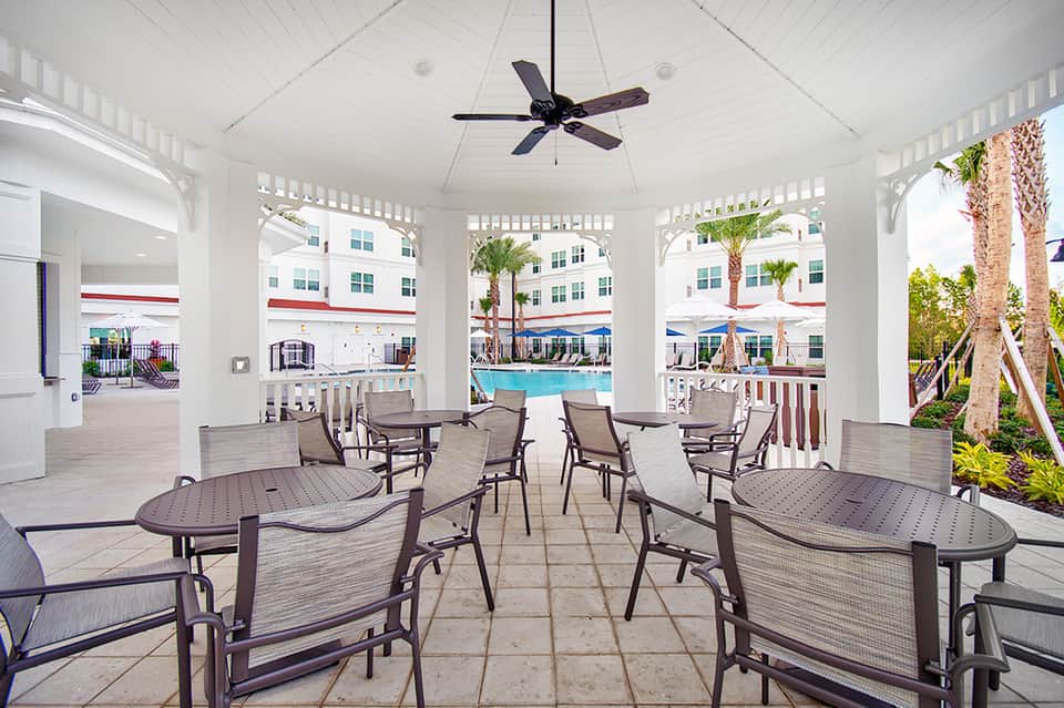 Covered poolside pavilion with lounge chairs, high ceiling, fan, and views of resort pool and palm trees