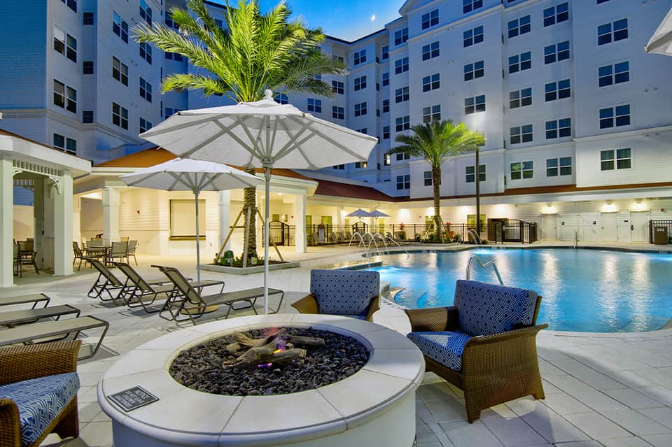 Modern resort pool area at night with illuminated water, fire pit, and contemporary architecture