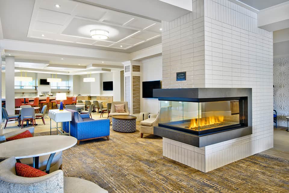 Contemporary hotel lobby with fireplace, colorful seating, coffered ceiling, and modern furnishings