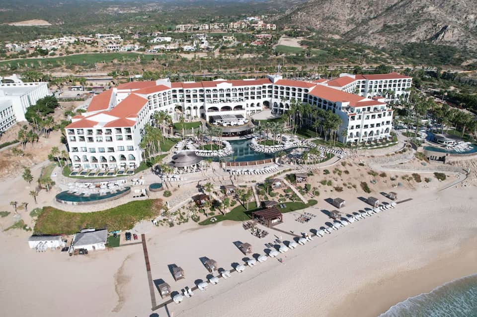 Aerial view of large beachfront resort complex with red roofs and mountain backdrop