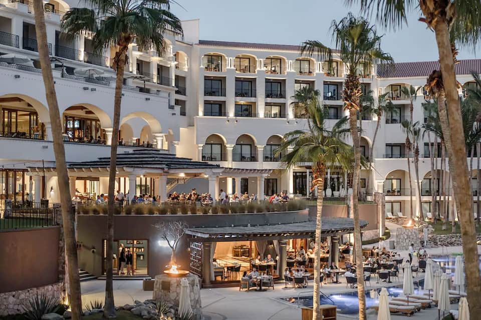Modern hotel building with arched windows, terrace dining, and palm trees