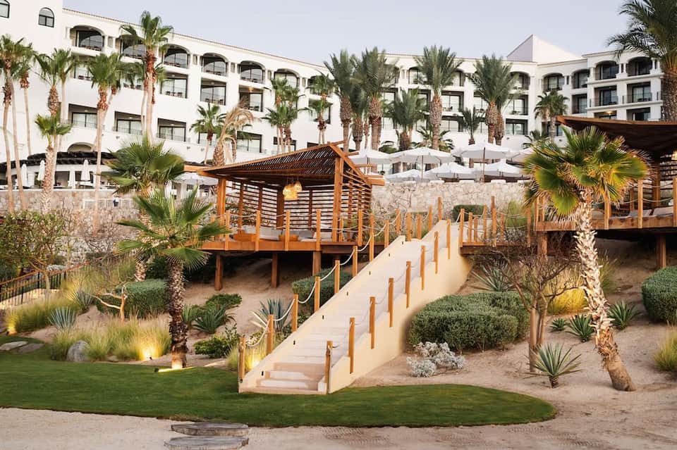 Beachfront resort with white buildings, wooden boardwalk, desert landscaping, and palm trees