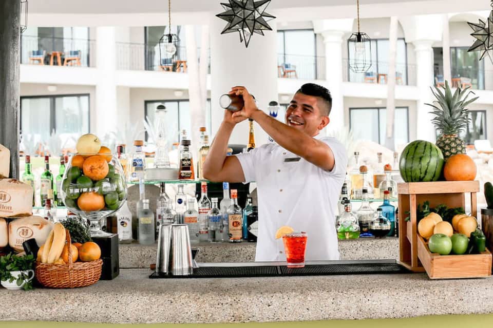 Resort bartender mixing cocktail at outdoor bar with tropical fruits and spirits display