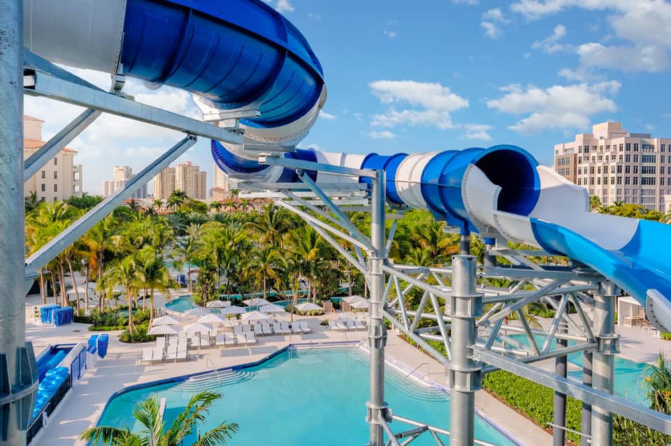 Blue water slide at resort pool with city skyline and palm trees in background