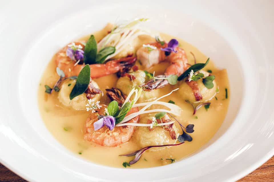 Gourmet plated shrimp dish with edible flowers and microgreens on white plate