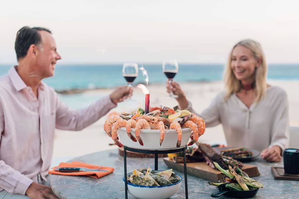 Couple toasting wine by beach table with seafood platter and ocean backdrop