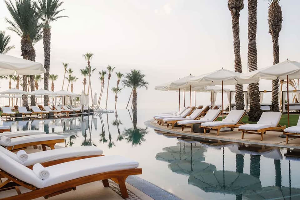 Beachfront infinity pool with palm trees, white umbrellas, and serene water reflections