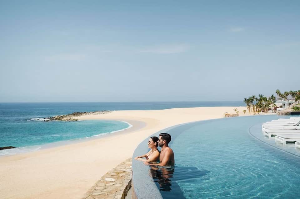 Couple relaxing in infinity pool overlooking pristine beach and ocean at luxury resort
