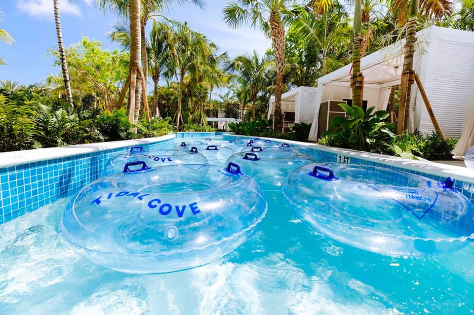 Tropical resort pool with clear blue water and branded float tubes surrounded by palm trees and white cabanas