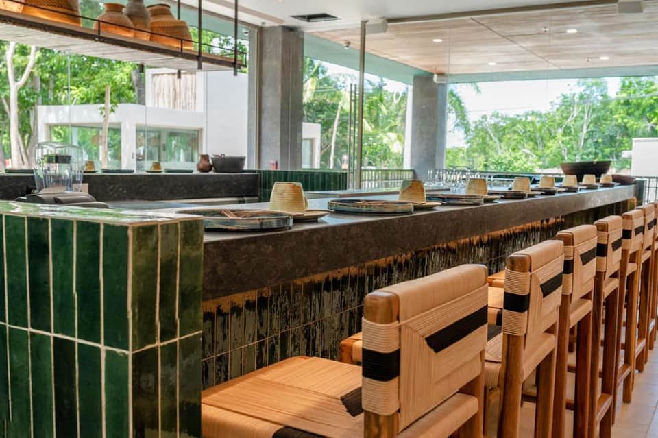 Contemporary restaurant with green tiled bar, wooden stools, and floor-to-ceiling forest views
