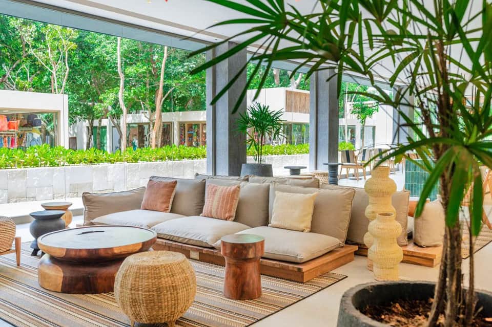 Contemporary outdoor lounge with sectional seating, wooden tables, and lush greenery
