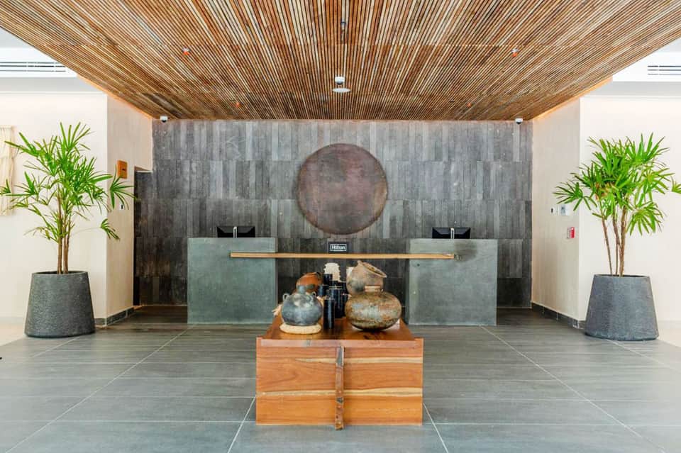 Contemporary hotel lobby with wooden slat ceiling, stone accent wall, and decorative pottery