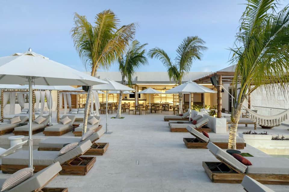 Beachfront resort with white umbrellas, lounge chairs, palm trees, and ocean