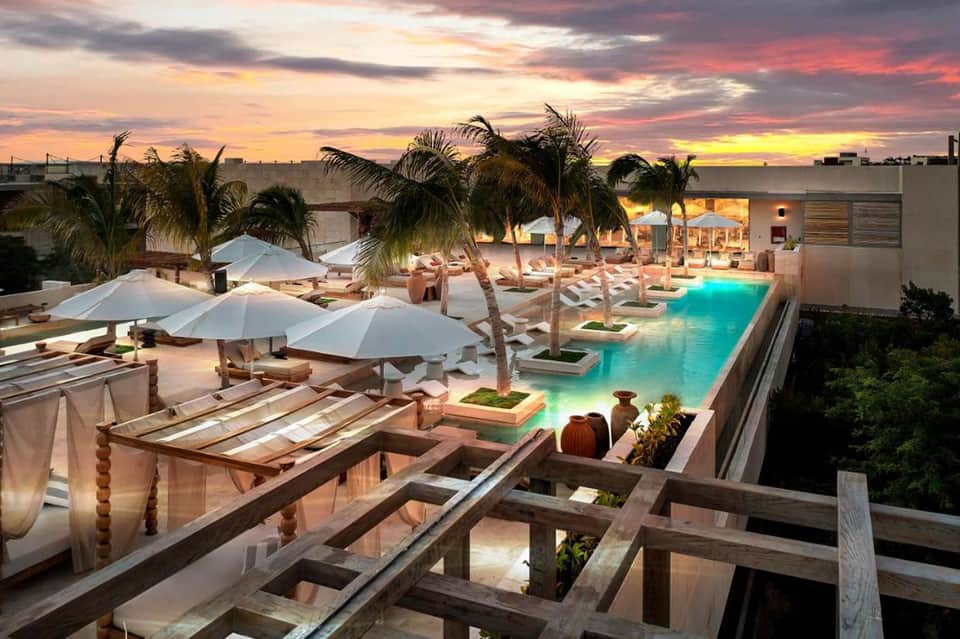 Beachfront resort pool illuminated at dusk with umbrellas and palm trees