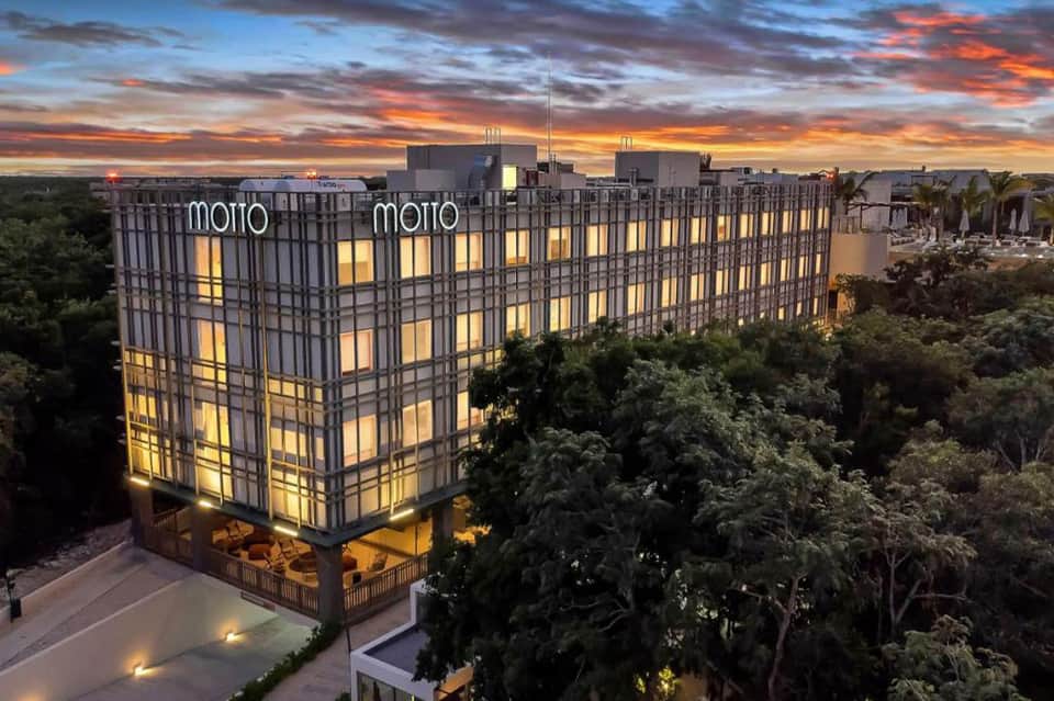 Motto hotel building illuminated at dusk with palm trees