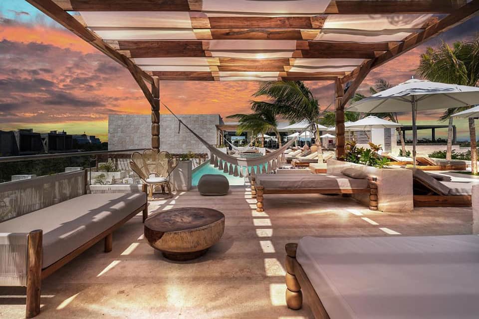 Sunset view of beachfront lounge area with hammocks, wooden pergola, and comfortable seating
