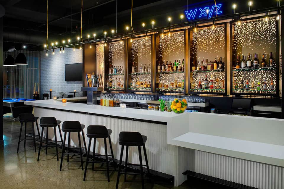 Contemporary bar with white counter, black stools, and extensive illuminated bottle display
